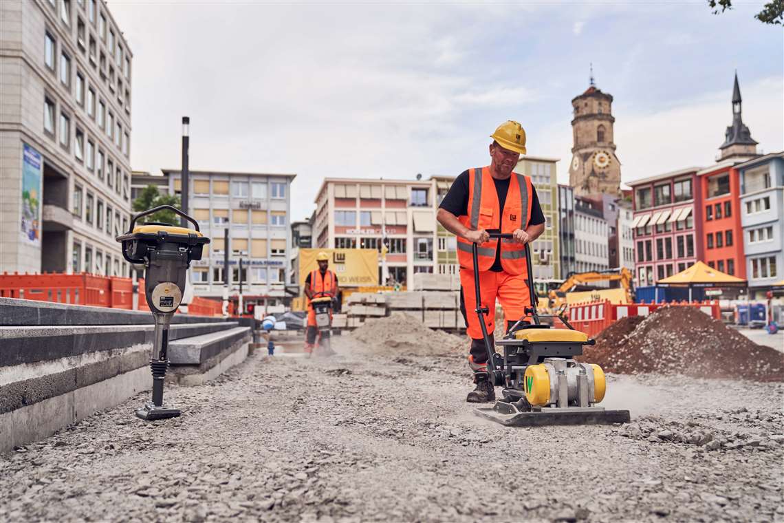 Construction site worker using a vibratory plate to compact soil