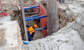 A worker digging in a trench with shoring protection
