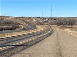 A road in Texas set against a blue sky with two white pick-up trucks approaching in the distance.