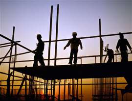 Construction workers in silhouette against a sunset on scaffolding