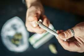 Close-up photo of two hands, one holding a marijuana joint and the other holding a cigarette lighter.