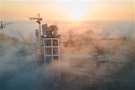 Aerial view of cement factory with high concrete plant structure and tower crane at industrial production site on foggy morning.