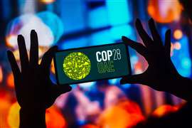 Silhouette of hands holding a smartphone displaying the COP28 logo.