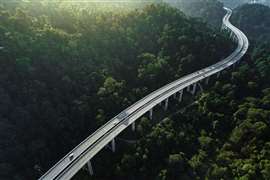 Aerial shot of car using elevated highway road across a green forest in the morning with mist