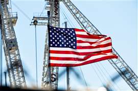 A stars and strips flag flying in front of construction cranes to signify US construction
