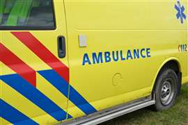 Dutch Ambulance logo on the side of a parked medical van. Ambulance sign on yellow vehicle with red and blue stripes.