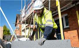 A Wates worker, in branded PPE, saws into a block of insulation.
