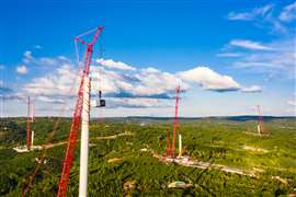 Cranes installing a series of large wind turbines in a green landscape.
