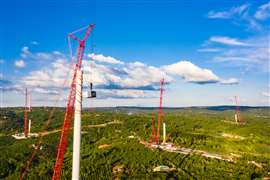Grues installant une série de grandes éoliennes dans un paysage verdoyant.