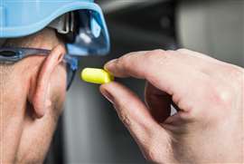 A construction worker placing a standard foam ear plug into their ear.