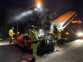 Ein Straßenbauteam arbeitet nachts mit dem Asphaltfertiger Cat AP500