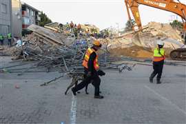 A rescue worker walks with a dog past the site where construction workers are trapped under a building that collapsed in George, South Africa, 7 May 2024.