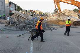 Un trabajador de rescate camina con un perro junto al lugar donde los trabajadores de la construcción están atrapados debajo de un edificio que se derrumbó en George, Sudáfrica, el 7 de mayo de 2024.