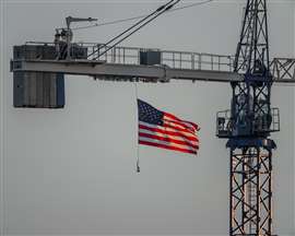 United States flag gracefully flying, back lit by setting sun and hanging from crane on a construction site