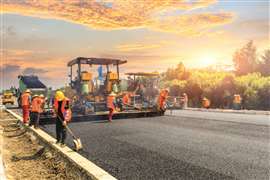 Labourers work alongside a machine paver. (Image: Adobe Stock)