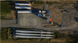 Uma torre de turbina eólica e pás rotativas jazem perto de uma fundação, prontas para montagem na Romênia. Imagem: Strabag