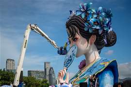 A construction worker uses powered access equipment to work on the eye of a large woman Hanfu sculpture in front of the Hong Kong skyline on 28 September 2025. (Image: Vernon Yuen/Nexpher Images via Zuma Press Wire).