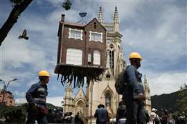 Construction workers walk past the installation "Pulled by the Roots" by Argentine artist Leandro Erlich during the BOG25 International Art Biennial at Plaza de Lourdes, in Bogota, Colombia. (Image: Reuters/Nathalia Angarita).