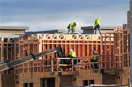 Pekerja konstruksi membingkai bangunan tempat tinggal multi-unit, mengerjakan perancah dan atap sebagai bagian dari proyek pembangunan perumahan aktif di East Mesa, Arizona