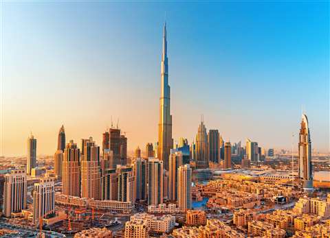 Sunlight catches one side of the Burj Khalifa in Dubai. The building is photographed at a distance and surrounded by other tall building in the area.